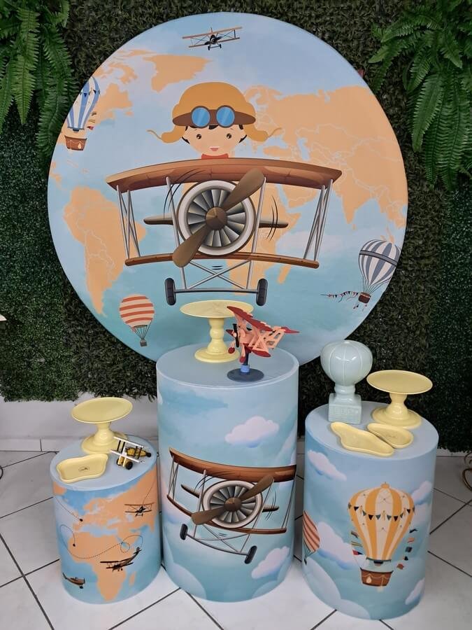 Kit completo de decoração afetiva e lúdica no estilo "Pegue e Monte" com a temática Aviador. Baseado na imagem real, o conjunto conta com um painel redondo gigante ilustrando um lindo macaquinho aviador em seu avião vintage sob um mapa-múndi e balões de ar quente. Acompanha trio de cilindros totalmente envelopados e coordenados com o tema (estampas de nuvens, aviões e mapas), suportes elevados para doces em tom amarelo suave, miniatura colecionável de avião de madeira e um vasinho decorativo em formato de balão de ar quente cerâmico. Kit completo de decoração afetiva e lúdica no estilo "Pegue e Monte" com a temática Aviador. Baseado na imagem real, o conjunto conta com um painel redondo gigante ilustrando um lindo macaquinho aviador em seu avião vintage sob um mapa-múndi e balões de ar quente. Acompanha trio de cilindros totalmente envelopados e coordenados com o tema (estampas de nuvens, aviões e mapas), suportes elevados para doces em tom amarelo suave, miniatura colecionável de avião de madeira e um vasinho decorativo em formato de balão de ar quente cerâmico.<br />