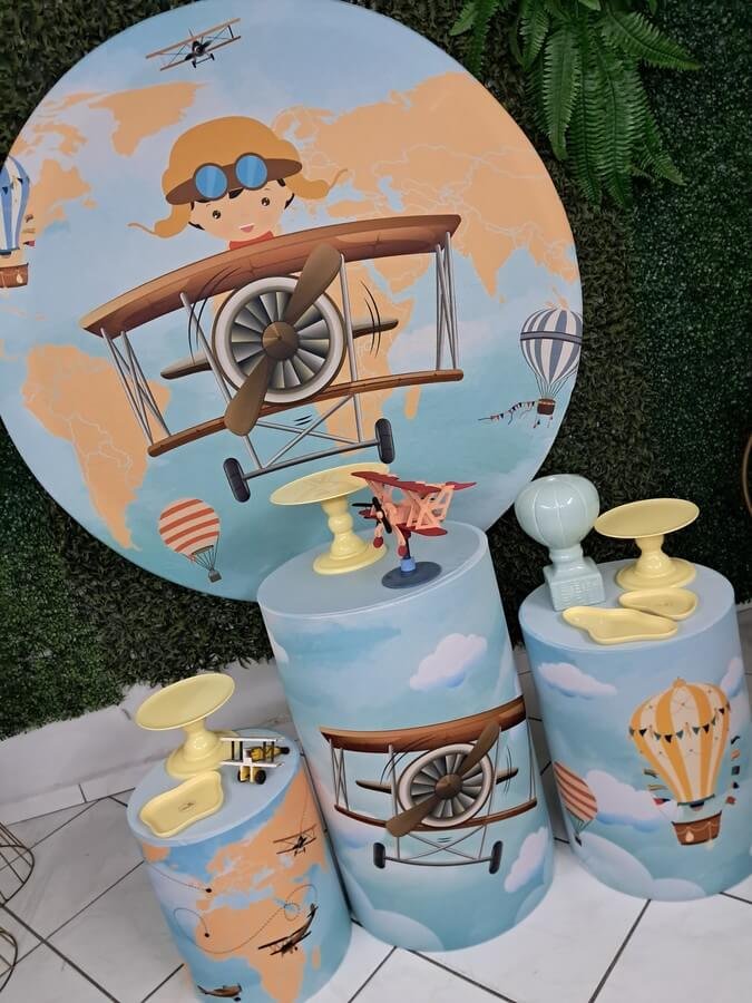 Kit completo de decoração afetiva e lúdica no estilo "Pegue e Monte" com a temática Aviador. Baseado na imagem real, o conjunto conta com um painel redondo gigante ilustrando um lindo macaquinho aviador em seu avião vintage sob um mapa-múndi e balões de ar quente. Acompanha trio de cilindros totalmente envelopados e coordenados com o tema (estampas de nuvens, aviões e mapas), suportes elevados para doces em tom amarelo suave, miniatura colecionável de avião de madeira e um vasinho decorativo em formato de balão de ar quente cerâmico. Kit completo de decoração afetiva e lúdica no estilo "Pegue e Monte" com a temática Aviador. Baseado na imagem real, o conjunto conta com um painel redondo gigante ilustrando um lindo macaquinho aviador em seu avião vintage sob um mapa-múndi e balões de ar quente. Acompanha trio de cilindros totalmente envelopados e coordenados com o tema (estampas de nuvens, aviões e mapas), suportes elevados para doces em tom amarelo suave, miniatura colecionável de avião de madeira e um vasinho decorativo em formato de balão de ar quente cerâmico.<br />